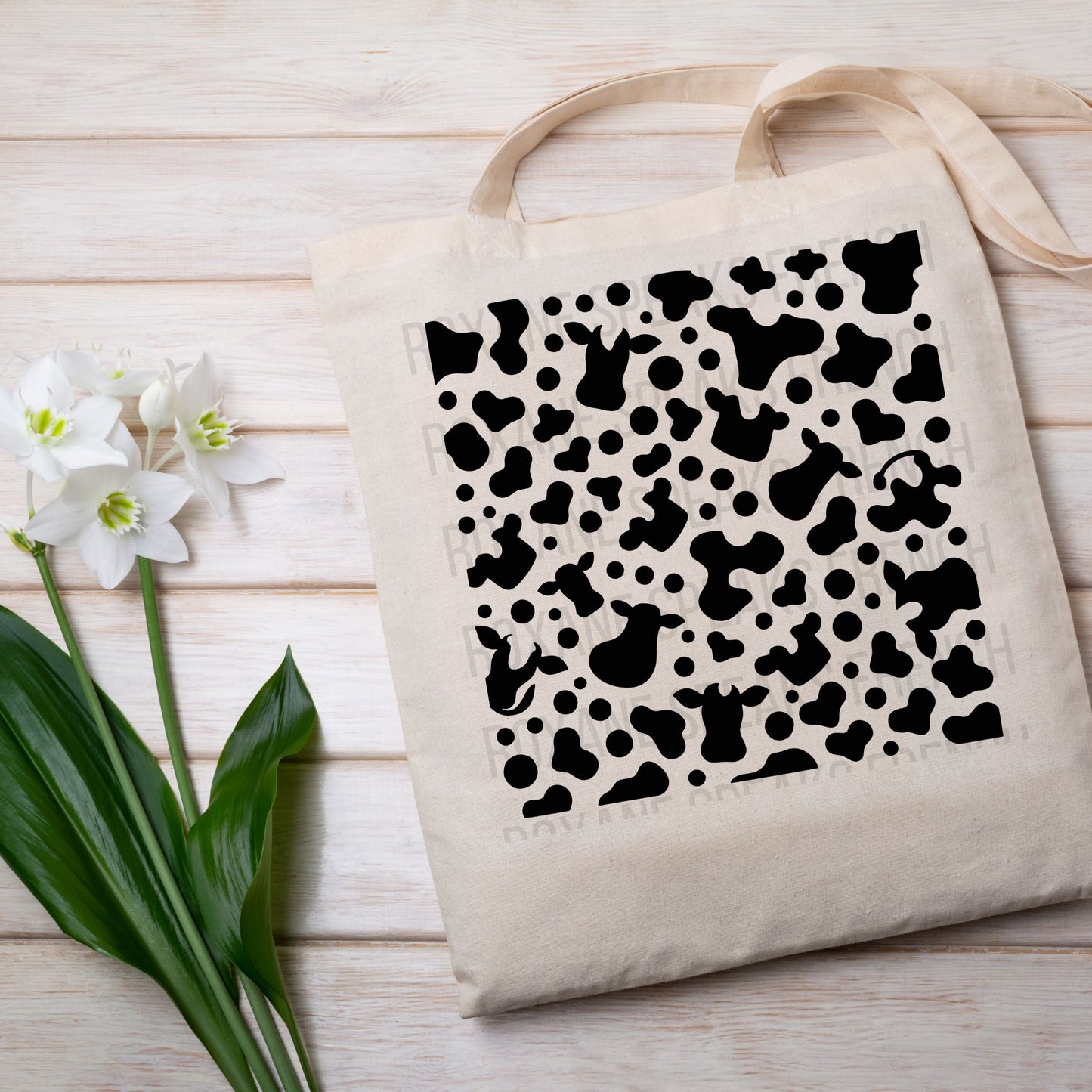 The image shows a tote bag with a cow print design, placed on a wooden surface. The design on the tote bag is reminiscent of the black and white pattern often associated with cows, and it makes a bold, playful statement.